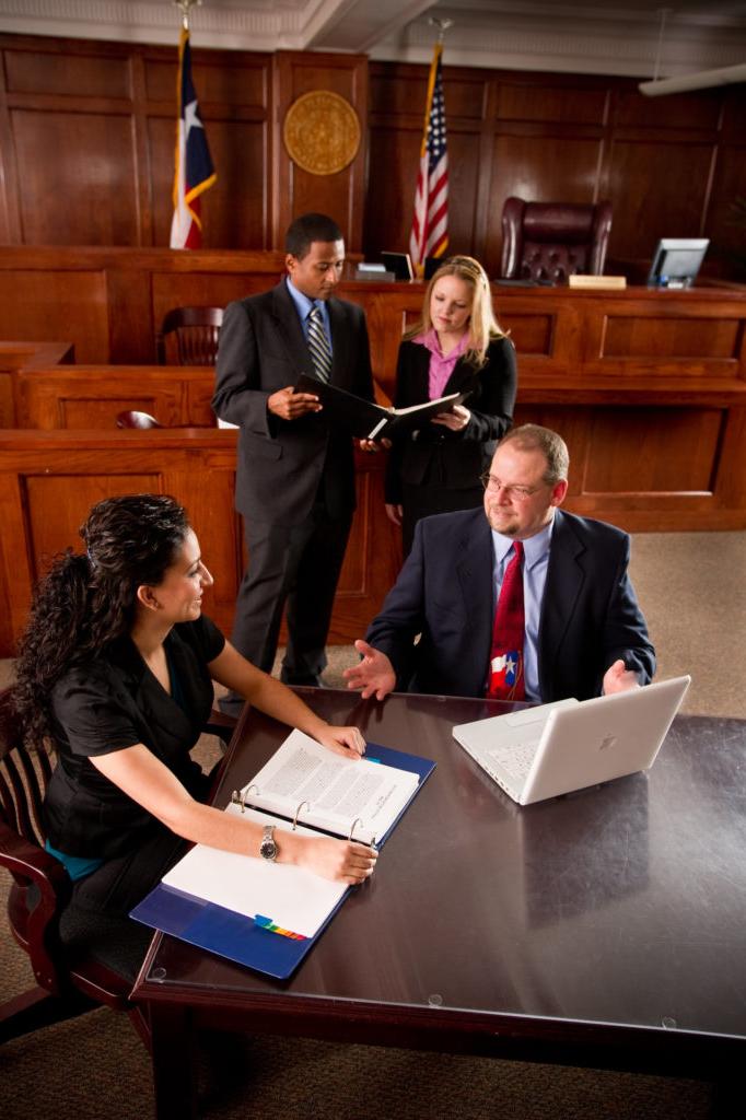 Man and Woman at table in courtroom with another man and woman discussing a case in the background