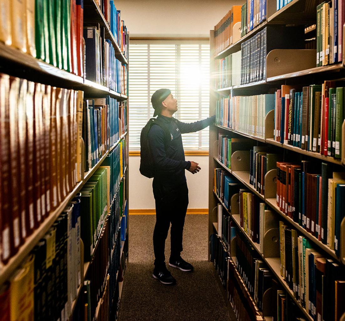 Male student looking for a book in the library.