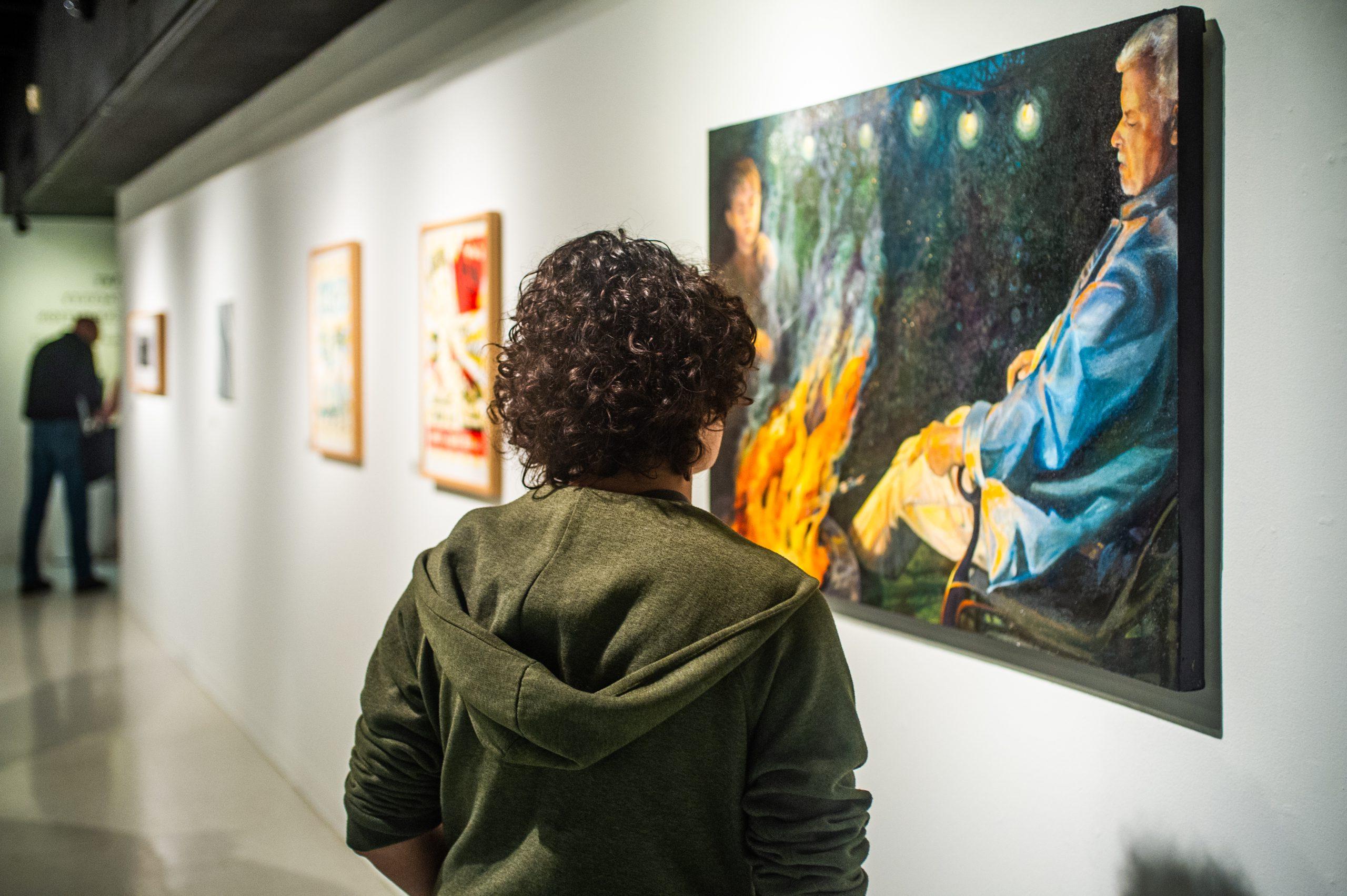 A male student looking at a painting in a art gallery.